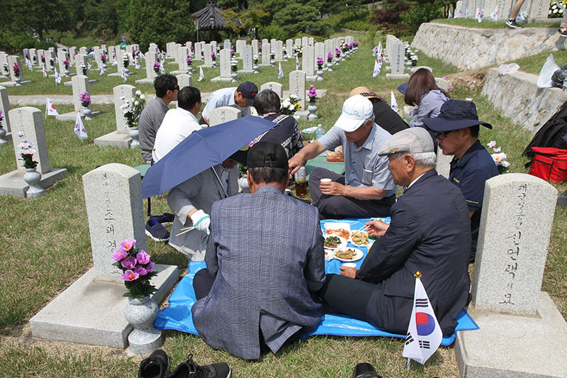 チャン・ラッカさんの墓碑と、供えられた写真。下は墓碑を囲んで食事をしながら語り合う遺族たち。