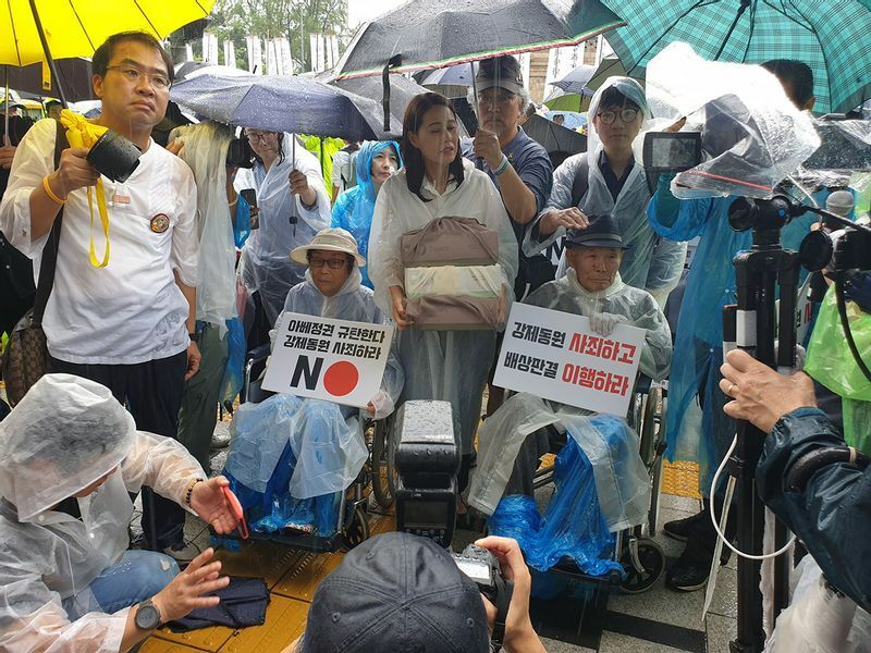 19年8月、ソウル日本大使館前で会見する強制徴用被害者の梁錦徳(ヤン・グムドク、中央左)さんと李春植(イ・チュンシク)さん。93歳の梁さんは「謝罪なくしては死んでも死にきれない」と明かす。筆者撮影。