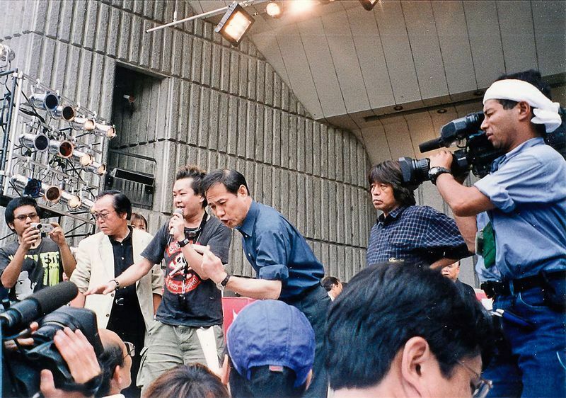 2001年、日比谷野音集会で壇上から叫ぶ鈴木さん。後ろは森達也さん（筆者撮影）