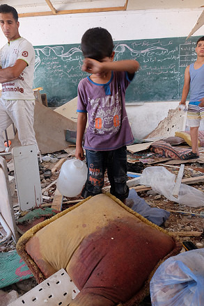 破壊された国連運営の学校の教室。血染めのクッションの前で少年が涙ぐんでいた。