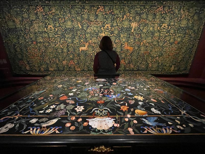 手前はフィレンツェで17世紀初頭に作られた大理石象嵌細工のテーブル。壁面には、1530–1535年にフランドル地方で製作されたタピスリー。「Mille fleurs（ミルフルール＝千の花）」がテーマ