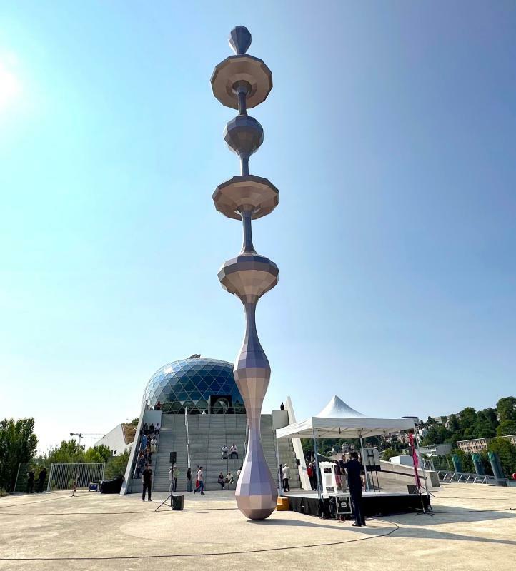 名和さんの彫刻作品「Ether(equality)」。奥のガラスの球体のような建物が坂茂氏設計の音楽堂「ラ・セーヌ・ミュージカル」。彫刻の多面的な構成が音楽堂の外観と呼応している