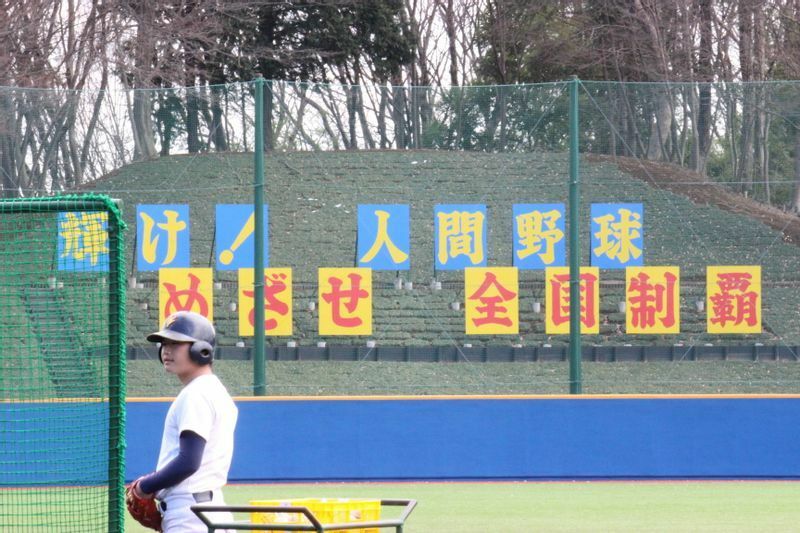 「輝け！人間野球　めざせ全国制覇」という標語が創価大学ワールドグラウンドには掲げられている（筆者撮影）