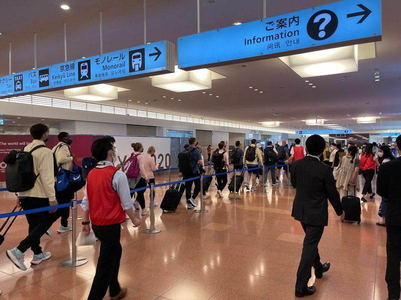 羽田空港国際線到着ロビーを通り過ぎる米国選手団。その右側にはスーツケースを引いて歩く一般客の後ろ姿も見られる（高橋浩祐撮影）