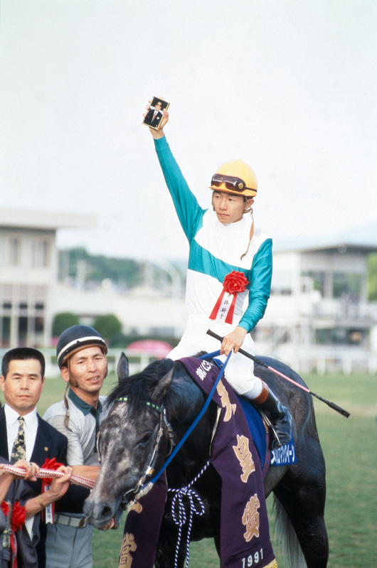 第103回天皇賞優勝のメジロマックイーン。武豊騎手は故・北野豊吉氏の写真を右手に持ち、大きく掲げている。(提供:競馬博物館)
