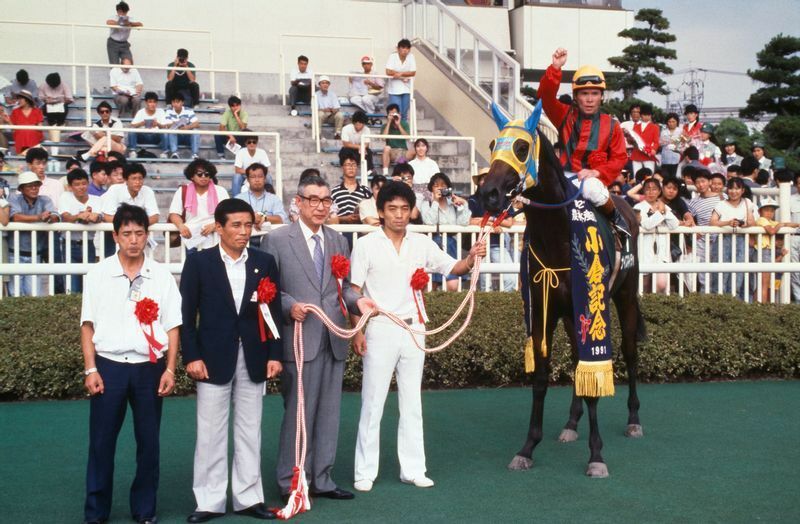 1991年、小倉記念を優勝したナイスネイチャの口取りの後継。馬上は松永昌博騎手(現・調教師)、馬の左隣より馬場秀輝厩務員。豊嶌泰三オーナー、松永善晴調教師、松永厩舎調教助手/ＪＲＡ