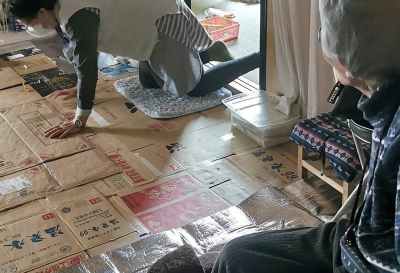 静岡市葵区の住宅で床の状態などを見る「地域支え合いセンター」のスタッフ。昨年の浸水で応急対応は終わったが、床が冷えるためダンボールなどを敷き詰めているという。（3月17日、しぞ〜か・まめっ隊提供）