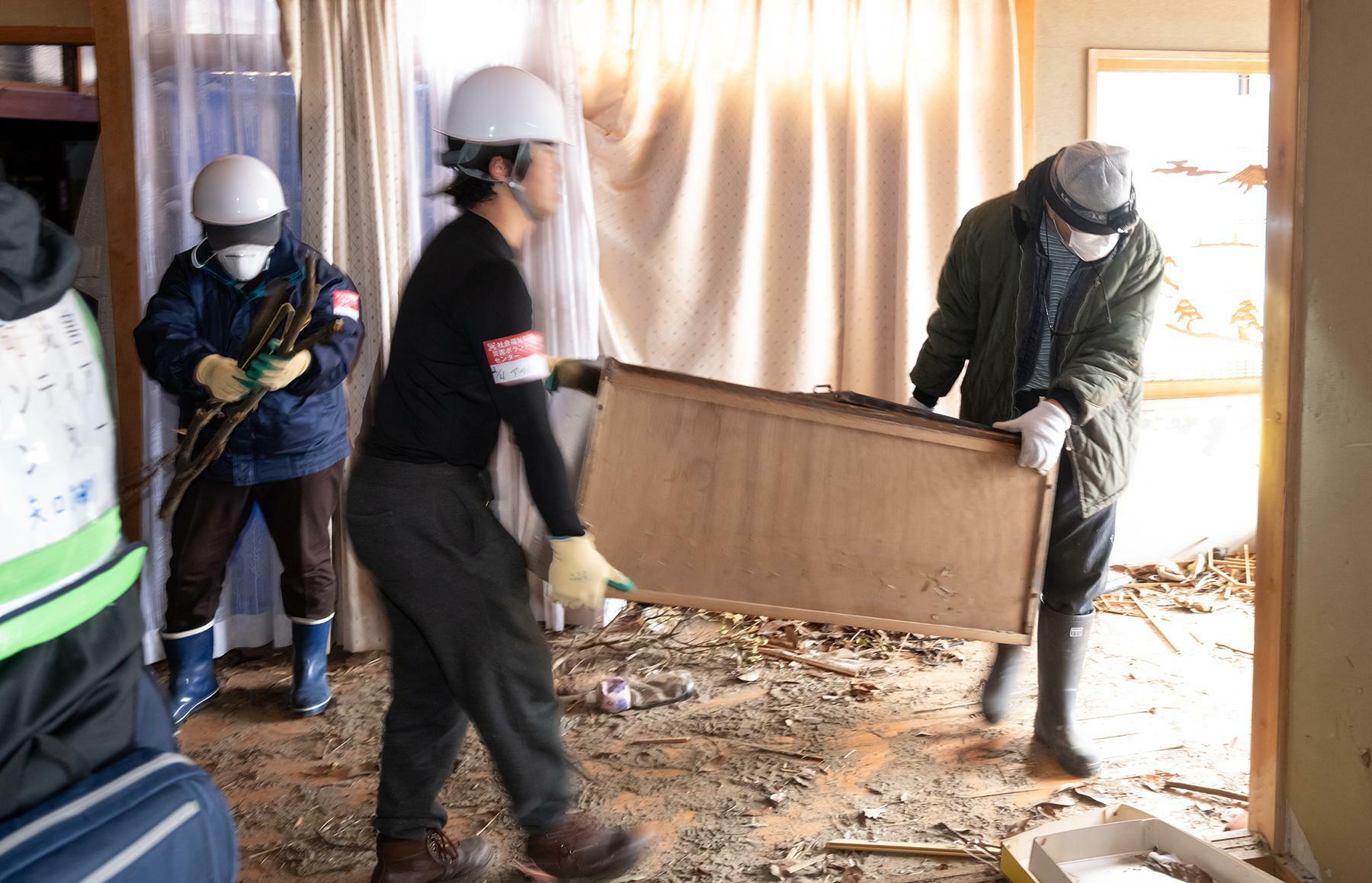  津波をかぶった1階の家財道具を運び出すボランティアと滝田さん＝2月4日、夏目健司撮影