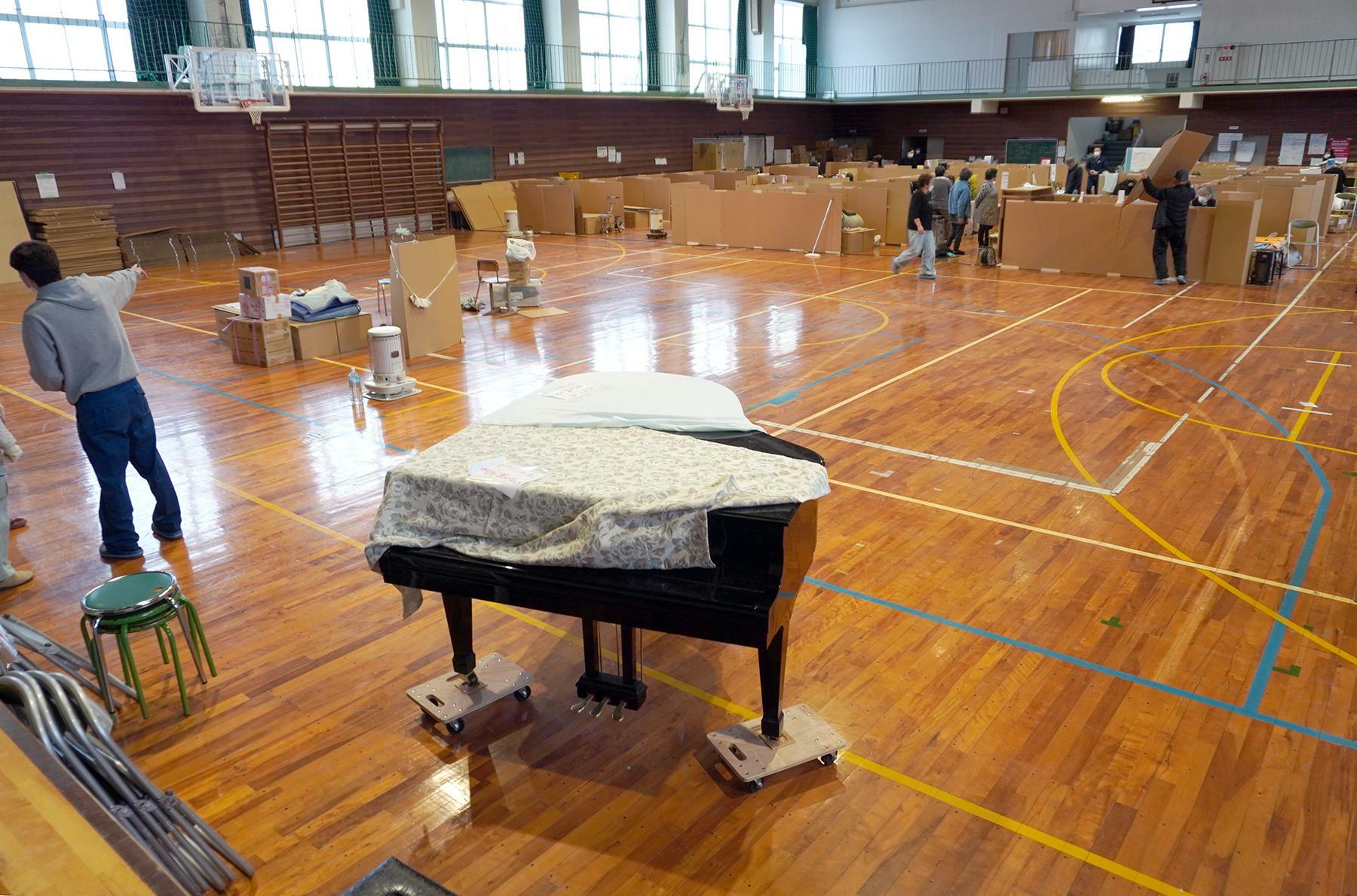 松波中学校の体育館では、小中学校の卒業式のために段ボールの避難所スペースを縮小し、舞台側にピアノなどを置く作業が行われていた＝3月3日、筆者撮影