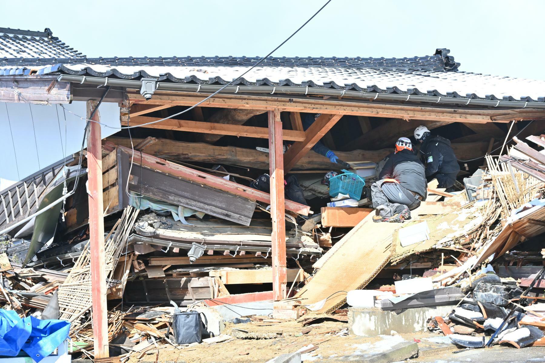 崩れ落ちた2階の屋根の下で作業するボランティア。左手の2本の細い柱もボランティアが支えのために立てたという＝3月2日、加藤直人撮影