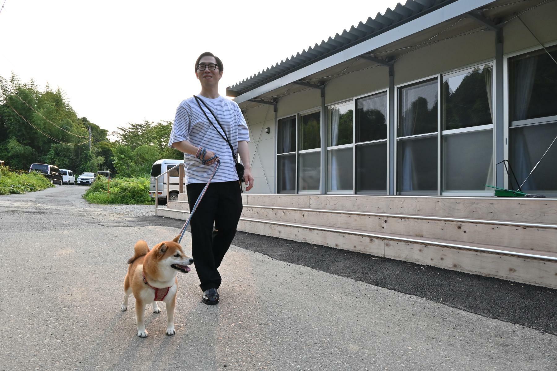 仮設団地の集会所の前を歩く山下さん。普段、ミクの散歩は父の担当だという＝7月13日、加藤直人撮影