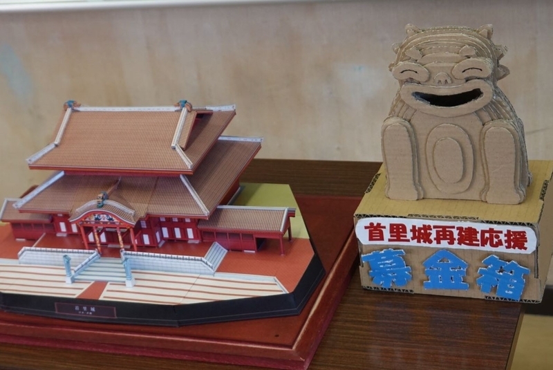 石井さんが制作した“シーサー募金箱”とペーパークラフトの首里城（筆者撮影）