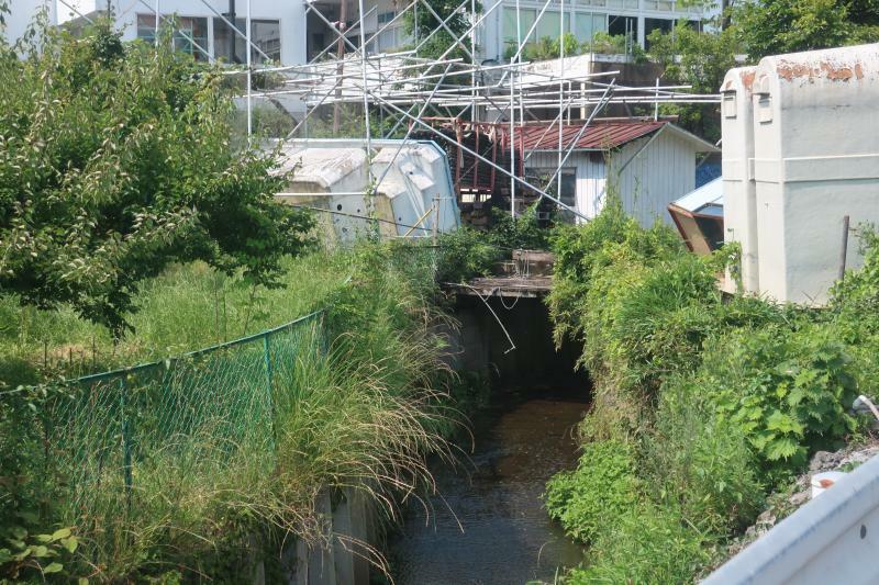 町管理の河川を建物が被さり塞いでいる部分の近景を町道の橋から撮影。普通に考えてこのような占有を町が許可するわけがないのが一目瞭然である。