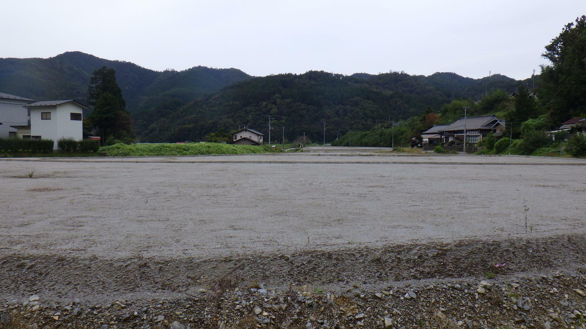 東山町の休耕中の農地。上記リンクの岩手日報さんの記事の写真と同じ「1階が灰色で2階が白色の建物」が背後の中央付近にあることから、白い農地と判断される。