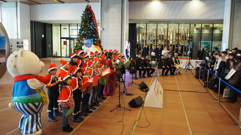 出発に先立って旭川駅で行われたセレモニー。「安平町雪だるま大使」の高橋涼子さんと歌う子どもたち。