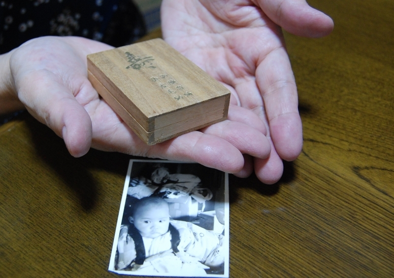 添野さんのへその緒と誕生時の毛髪が入った箱。乳児期の写真は本人（筆者撮影）