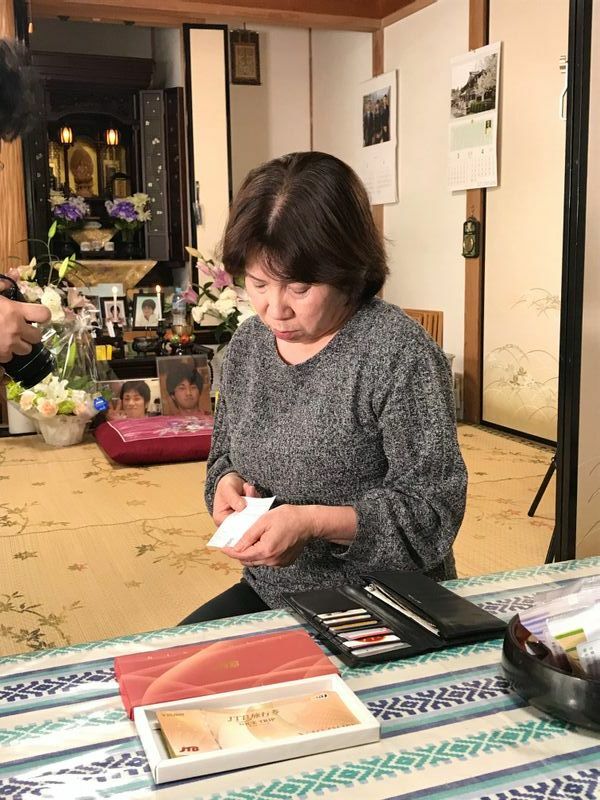 隆史さんが亡くなる1週間前、父親の還暦祝いに贈ってきた旅行券を見つめる母親のるり子さん。遺品の財布には、2日前に東京から発送した際の書留の控えもそのまま残されていた（筆者撮影）
